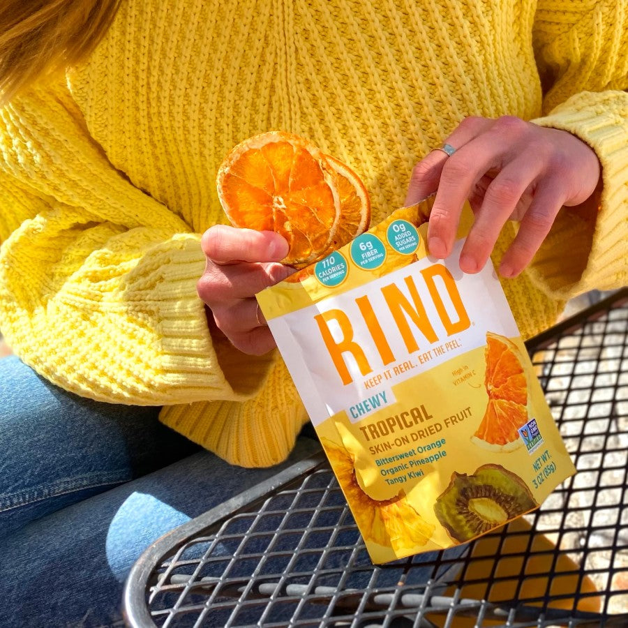 Person In Bright Yellow Sweater Enjoying Chewy Skin-On Dried Fruit RIND Snacks Tropical Blend